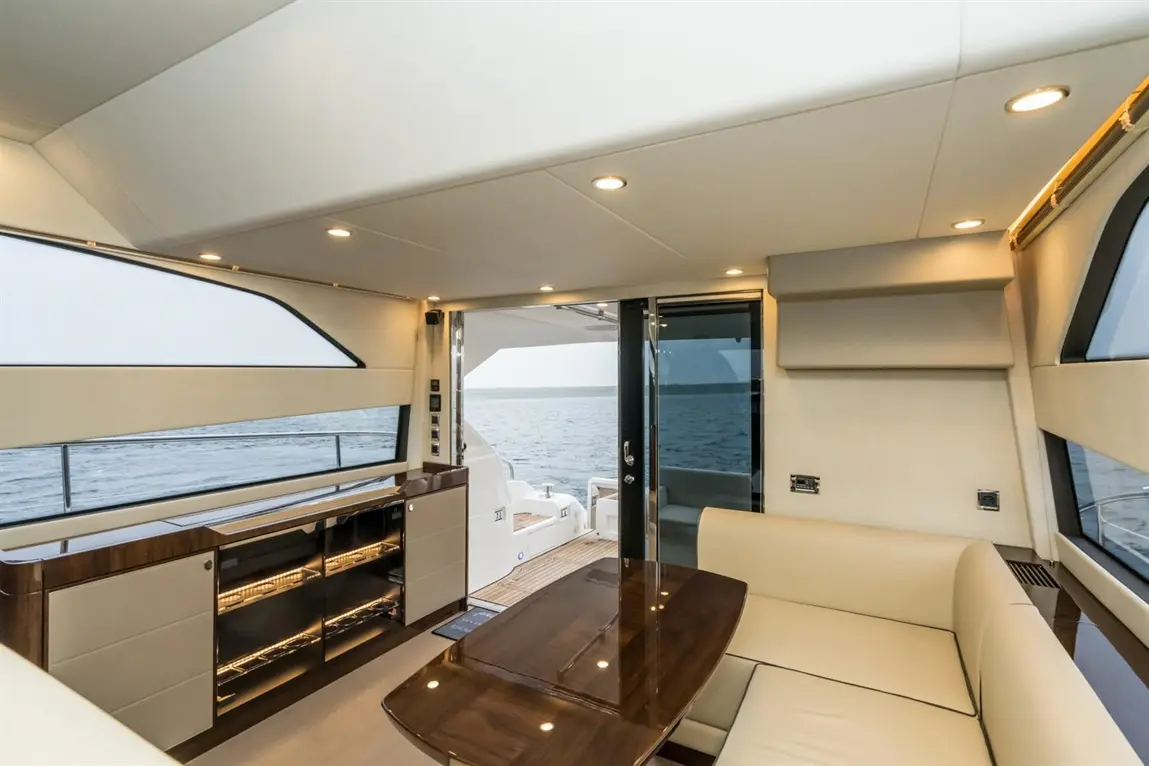 Modern yacht interior featuring a seating area, wooden table, and glass doors leading to the deck with sea views.